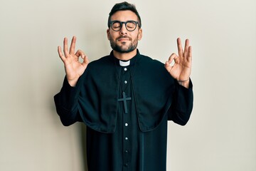 Young hispanic man wearing priest uniform standing over white background relax and smiling with...