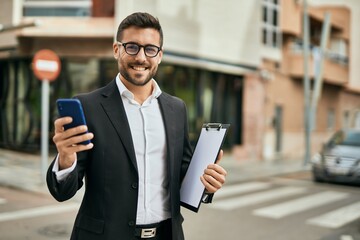 Young hispanic businessman smiling happy using smartphone at the city.