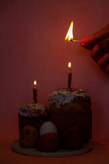 Hand lights  candle on easter kulich on pink background