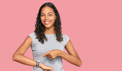 Young african american girl wearing casual clothes in hurry pointing to watch time, impatience,...