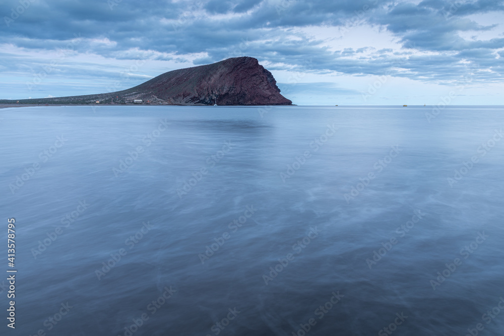 Poster beautiful scenery of a blue sea with a large rock in the background under the cloudy sky