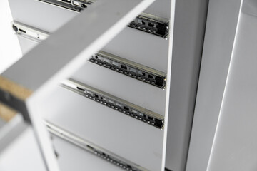 Stainless telescopic bayonet drawer slide guides, installed on a kitchen cabinet from gray chipboard. Accessories for carpentry used in the construction of furniture. Custom kitchen installation.