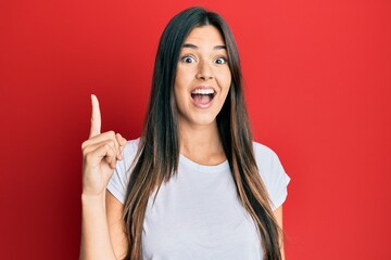 Young brunette woman wearing casual white tshirt over red background pointing finger up with successful idea. exited and happy. number one.