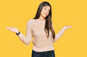 Young brunette woman wearing casual winter sweater clueless and confused expression with arms and hands raised. doubt concept.