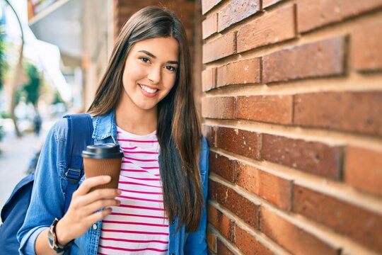 Young hispanic student girl smiling happy drinking coffee at the city.