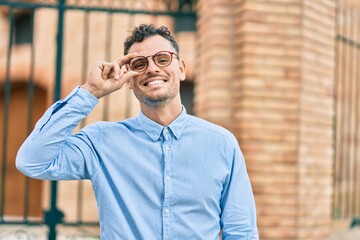 Young hispanic businessman smiling happy touching his glasses at the city.