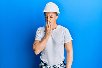Handsome young man wearing builder uniform and hardhat bored yawning tired covering mouth with hand. restless and sleepiness.