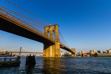 View of the Brooklyn Bridge seen from the East River Greenway in Manhattan with people standing under the bridge on an observation deck 