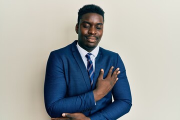 Handsome black man wearing business suit and tie hugging oneself happy and positive, smiling confident. self love and self care