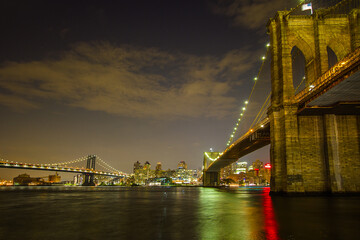 Fototapeta premium The view of the Brooklyn Bridge from Manhattan at night with the reflection of the city light on East River and Manhattan Bridge in the background 