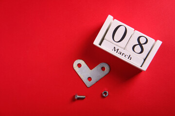 Metal corner in the form of a heart, a bolt and a nut, on a red background, a wooden calendar with the date of March 8
