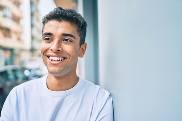 Young latin man smiling happy leaning on the wall at the city.