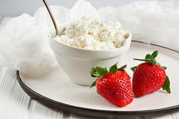 White bowl with fresh red ripe strawberries and natural cottage cheese, on white wooden table for fitness breakfast. Dietary product. The concept of healthy eating.