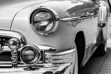 Retro-styled front of a classic car with round headlights in black and white image. The headlights...