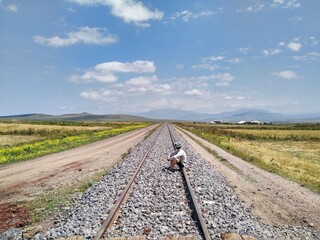 Cyclist sitting on the railway tracks looking towards the horizon