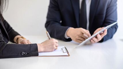 Businessman and businesswoman working in the office using a digital tablet and taking notes.