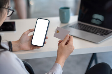 Image of a woman holding a smartphone and credit card in the office. Online shopping concept. Blank white screen. Mockup.