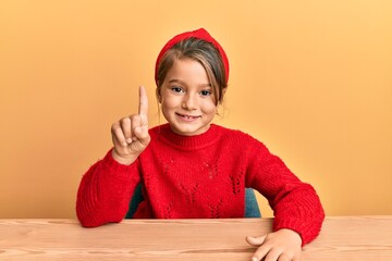 Little beautiful girl wearing casual clothes sitting on the table showing and pointing up with...