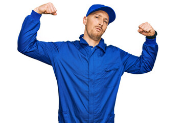 Bald man with beard wearing builder jumpsuit uniform showing arms muscles smiling proud. fitness concept.