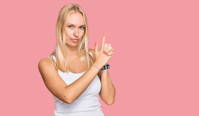 Young blonde girl wearing casual style with sleeveless shirt holding symbolic gun with hand gesture, playing killing shooting weapons, angry face