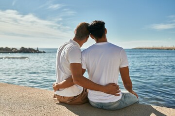 Young gay couple looking to the horizon sitting at the beach promenade. - obrazy, fototapety, plakaty