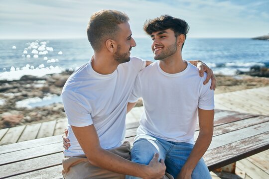 Young gay couple smiling happy sitting on the bench at the beach promenade.