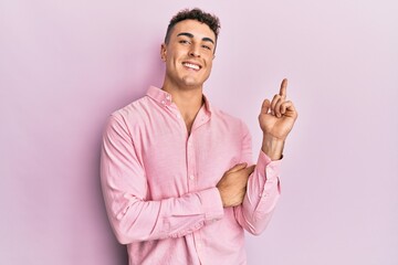 Hispanic young man wearing casual clothes with a big smile on face, pointing with hand and finger to the side looking at the camera.