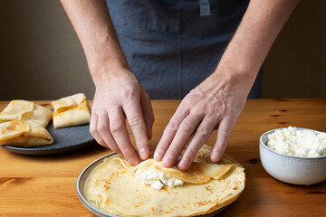 A man in the kitchen prepares a healthy breakfast of pancakes stuffed with fresh cottage cheese with sour cream and delicious fragrant honey.