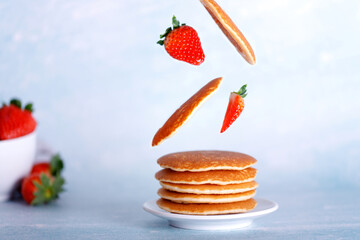 Plate with american pancakes with flying ingredients, pancakes, strawberries. Healthy food concept with copy space.