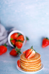 Tasty American pancakes with strawberries on white plate against blue background.