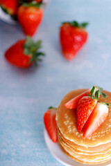 Tasty American pancakes with strawberries on white plate against blue background.