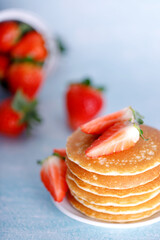 Tasty American pancakes with strawberries on white plate against blue background.