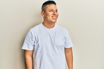 Young latin man wearing casual white t shirt looking away to side with smile on face, natural expression. laughing confident.