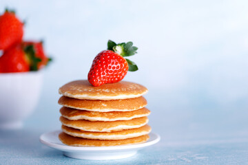Tasty American pancakes with strawberries on white plate against blue background.