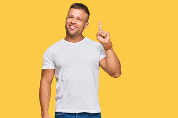 Handsome muscle man wearing casual white tshirt showing and pointing up with finger number one while smiling confident and happy.