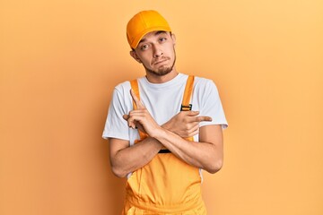 Hispanic young man wearing handyman uniform pointing to both sides with fingers, different direction disagree