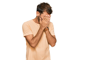 Handsome young man with beard wearing casual tshirt with sad expression covering face with hands while crying. depression concept.