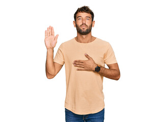 Handsome young man with beard wearing casual tshirt swearing with hand on chest and open palm, making a loyalty promise oath