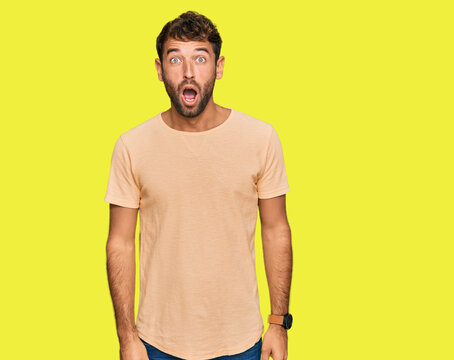 Handsome young man with beard wearing casual tshirt afraid and shocked with surprise and amazed expression, fear and excited face.
