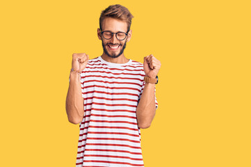 Handsome blond man with beard wearing casual clothes and glasses excited for success with arms...
