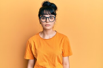 Young hispanic girl wearing casual clothes and glasses with serious expression on face. simple and...
