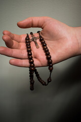 White hand holding a little brown wooden rosary 