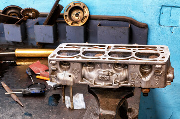 An old Cylinder head being repaired on a work table by a mechanic. In the blurred background other...