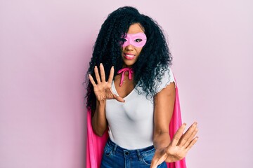 Middle age african american woman wearing super hero costume afraid and terrified with fear expression stop gesture with hands, shouting in shock. panic concept.