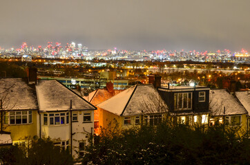 Night view of residential houses in Greenwich against distant illuminated Canary Wharf skyscrapers in winter, London, England