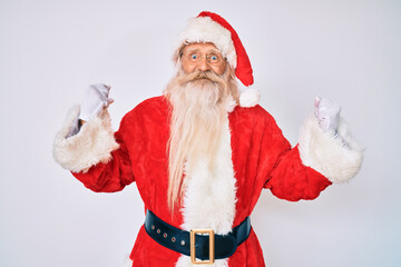 Old senior man with grey hair and long beard wearing santa claus costume with suspenders celebrating surprised and amazed for success with arms raised and open eyes. winner concept.
