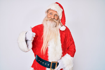 Old senior man with grey hair and long beard wearing santa claus costume with suspenders doing happy thumbs up gesture with hand. approving expression looking at the camera showing success.