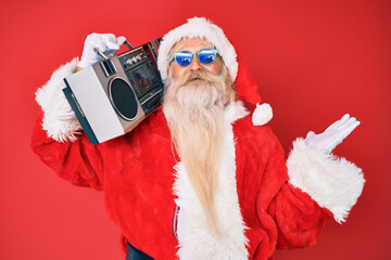 Old senior man wearing santa claus costume and boombox celebrating victory with happy smile and winner expression with raised hands