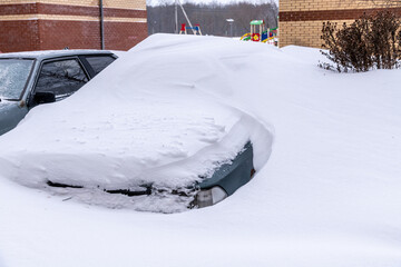 Cars in the parking lot near a residential building buried under the snow. Huge winter snowdrifts. Winter snow storm theme.