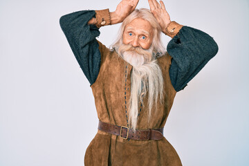 Old senior man with grey hair and long beard wearing viking traditional costume doing bunny ears gesture with hands palms looking cynical and skeptical. easter rabbit concept.
